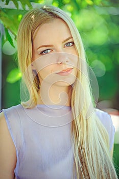 Attractive modest young girl with blond hair and natural make-up in purple dress outdoors, tenderness and softness on nature