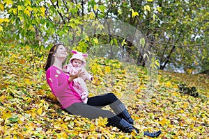 Attractive mother holding a baby girl playing with falling autumn leaves