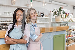 Attractive multiethnic waitresses looking at camera while standing together with arms crossed at cafe