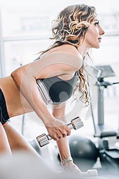 Attractive muscular fitness woman doing exercise with dumbbells in gym