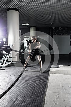 Attractive muscular man working out with heavy ropes. Photo of handsome man in sportswear. Crossfit