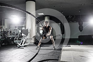 Attractive muscular man working out with heavy ropes. Photo of handsome man in sportswear. Crossfit