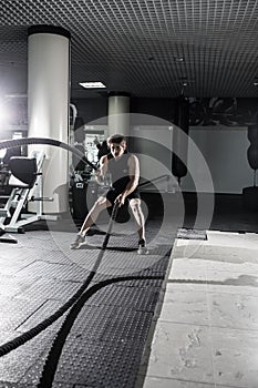 Attractive muscular man working out with heavy ropes. Photo of handsome man in sportswear. Crossfit