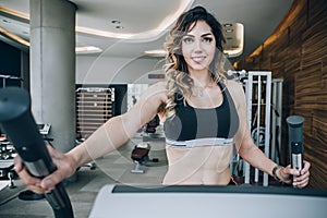 Attractive muscular smiling fitness woman running on treadmill in gym