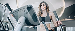 Attractive muscular smiling fitness woman running on treadmill in gym