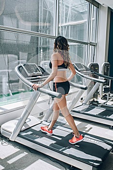 Attractive muscular smiling fitness woman running on treadmill in gym