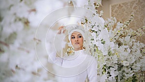 Attractive muslim bride with tiara in weddind dress in white flowers