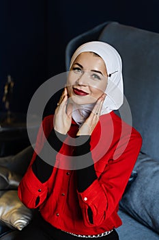 Attractive muslim caucasian girl weared head scarf is sitting on the sofa. Islam religion.