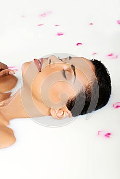 Attractive naked woman lying in a milk bath. With rose petal. Up