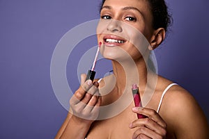 Attractive natural beauty African woman applies lipstick, hygienic lip gloss to plump lips, smiles toothy smile looking at camer,