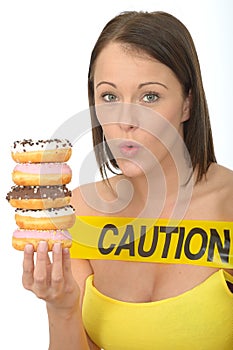 Attractive Natural Young Woman Holding a Pile of Iced Donuts with Caution Sign