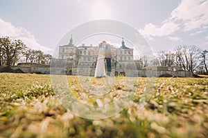 Attractive newlywed couple embracing at green sunny lawn near beautiful ruined baroque palace. Loving groom and charming