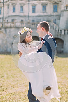 Attractive newlywed couple at green lawn near beautiful ruined baroque palace. Loving groom holding charming bride on