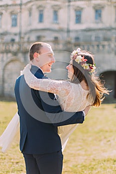Attractive newlywed pair at green sunny lawn near beautiful ruined baroque palace. Loving groom holding charming bride