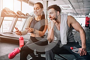 Attractive and nice people sitting on the sport bench and relaxing after long-term exercising. Girl shows something on