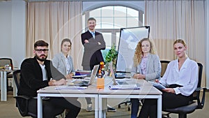 Attractive office team in front with the their team leader man looking straight to the camera and smiling large they