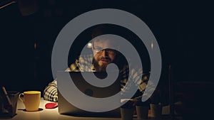 Attractive office worker working hard at his cabinet late at night, drinks tea and programming something on his computer