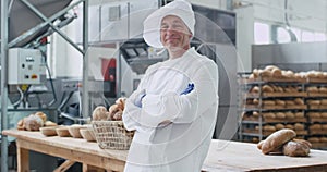 Attractive old baker man portrait smiling large in a bakery industry he crossed hands and enjoying the time at his work