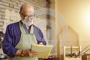 Attractive old carpenter working on designs in his workshop