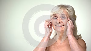 Attractive old lady doing facial exercises, anti-aging facebuilding for eyes