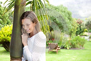 Attractive older woman leaning against tree and smiling