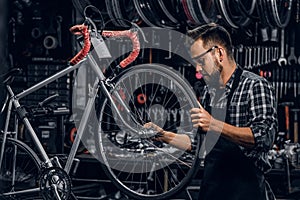 Attractive pensive man in protective glasses is repairing bicycle at his own workshop