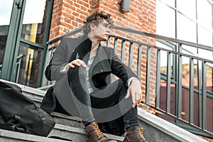 Attractive pensive man sitting on steps on red bricked building background.