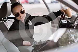 attractive policewoman with paper cup of coffee sitting in car and looking