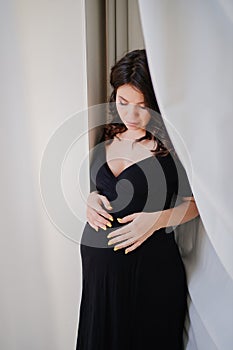 a attractive pregnant woman in a black dress by the window