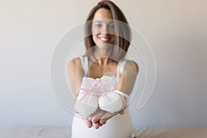 Attractive pregnant woman is sitting in bed, holding a baby bootees belly and smiling. Last months of pregnancy.Lifestyle indoors