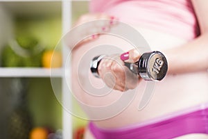 Attractive pregnant woman using a dumbbell while training