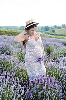 attractive pregnant woman in white dress touching hair and standing at violet photo