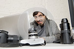 Attractive press photographer man working with laptop computer and desk full of photographic gear