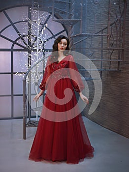 Attractive princess locked in tower, dressed in a luxurious red expensive long royal dress, her dark hair lies in waves