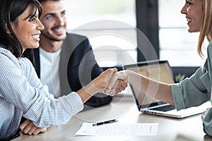 Attractive real-estate agent shaking hands with young couple after signing agreement contract in the office