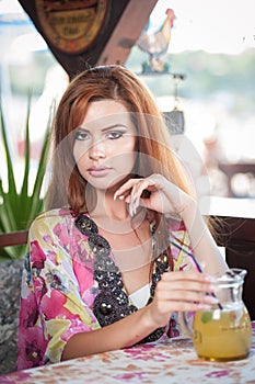 Attractive red hair young woman with bright colored blouse drinking lemonade on a terrace. Gorgeous redhead model drinking fresh