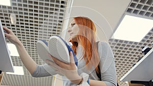 Attractive red haired woman chooses a sneakers in shoes store - shopping concept