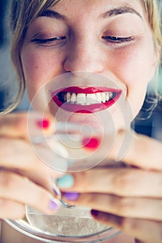 Attractive red lip stick and healthy white teeth: Blonde young woman with colorful nail polish is looking herself in the mirror