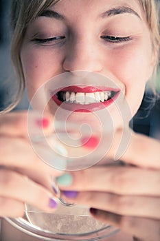 Attractive red lip stick and healthy white teeth: Blonde young woman with colorful nail polish is looking herself in the mirror