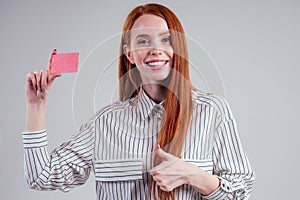 Attractive redhead caucasian businesswoman wearing striped shirt holding credit card studio white background black