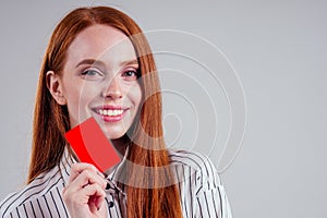 Attractive redhead caucasian businesswoman wearing striped shirt holding credit card studio white background black