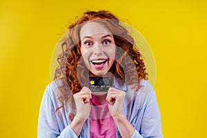 Attractive redhead curly ginger caucasian businesswoman wearing cotton shirt ,holding credit card studio yellow