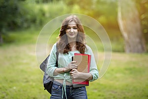 Attractive redhead student girl with backpack and workbooks posing at campus yard