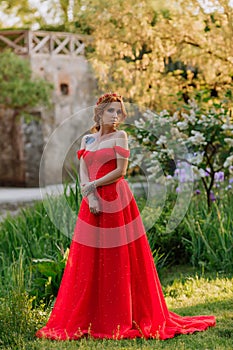 Attractive redhead woman in long red dress stays near the castle