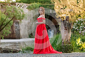 Attractive redhead woman in long red dress stays near the castle