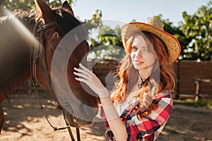 Attractive redhead young woman cowgirl in hat with her horse