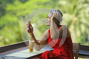 Attractive and relaxed 40s or 50s Asian woman with grey hair and stylish red dress using social media on inernet mobile phone at