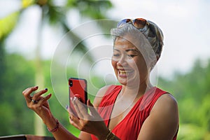 Attractive and relaxed 40s or 50s Asian woman with grey hair and stylish red dress using social media on inernet mobile phone at