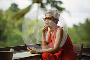 Attractive and relaxed 40s or 50s Asian woman with grey hair and stylish red dress using social media on inernet mobile phone at