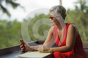 Attractive and relaxed 40s or 50s Asian woman with grey hair and stylish red dress using social media on inernet mobile phone at